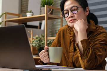 asian woman drink coffee cup and watching live streaming on laptop when work at home