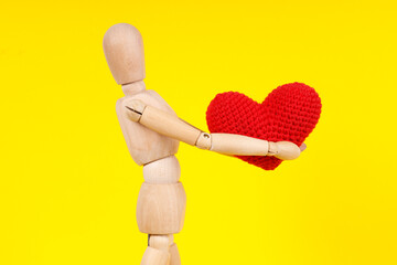 wooden man with a red heart in his hands on a yellow background