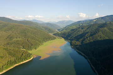 Fototapeta premium Aerial view of big lake with clear blue water between high mountain hills covered with dense evergreen forest