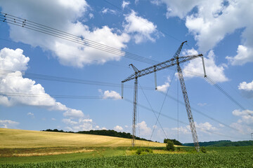 High voltage tower with electric power lines between green agricultural fields. Transfer of electricity concept