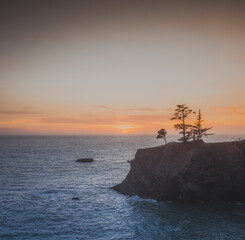 Sunset on natural bridges along the west coast of the Pacific Ocean, Oregon during the golden hour sunset - the sun's rays through the trees with dense vegetation. Beautiful seascape with rocks.