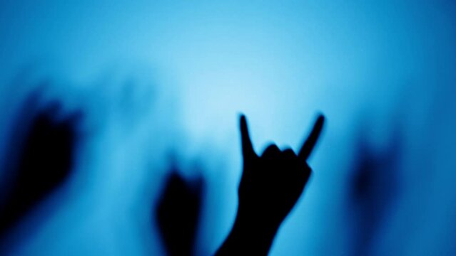 People showing rock and roll gesture with fingers isolated on blue background. Men making shadow silhouette with hand close-up, party and concert concept. 