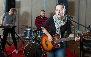 Rehearsal of music band. Female guitar player and singer practicing with band members in recording studio