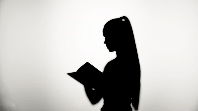 Shadow of woman reading book close-up, silhouette of female person reads story on white background. Education and learning concept.