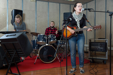 Rehearsal of music band. Pretty female guitar player and singer practicing with band members in recording studio