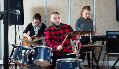 Music garage band with expressive male drummer rehearsing in rehearsal room