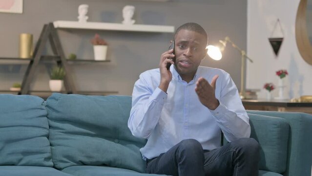 Angry African Man Talking on Smartphone on Sofa 