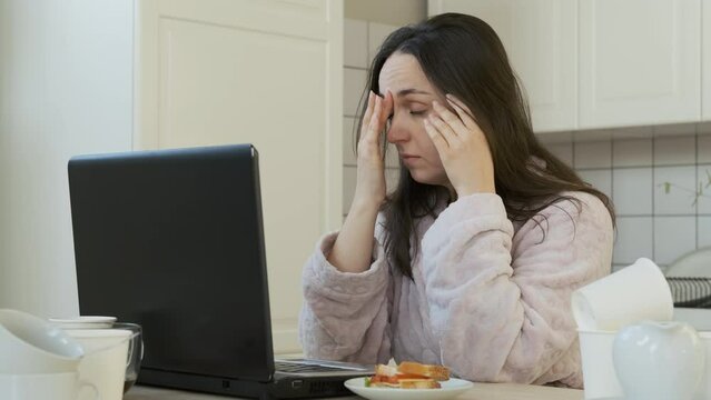 Tired Young Woman Overwhelmed with Freelance Job, Education or Working on Laptop in the Kitchen. Slow Motion. Working Overtime, Remote Work Concept
