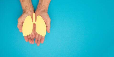 Lungs shape made from yellow paper on a palm old woman on a blue background