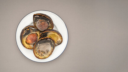 Rotten avocados cut in half on a white dish over a gray background