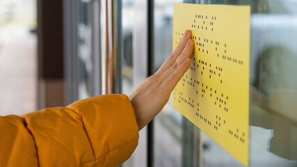 Close-up of a woman reading a braille lettering on a glass door.