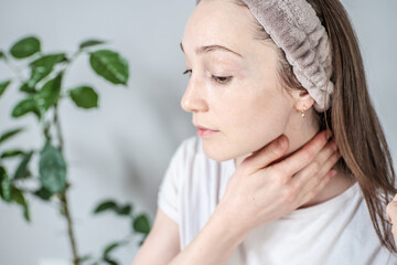 Young woman on the background of a green plant is doing a massage and smearing her neck with a natural organic cream or oil. Concept of spending time alone, relaxing, skin care and self care