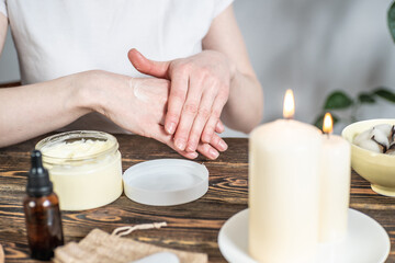 Obraz na płótnie Canvas Woman is smearing her hands with a natural organic cream doing a massage. Aroma lamp with essential oils and candles on the table. Concept of skin and self care in atmosphere of harmony and relaxation