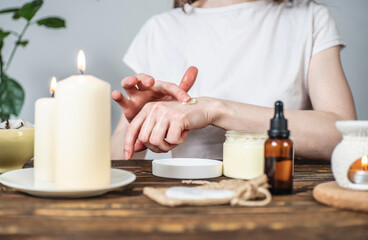Obraz na płótnie Canvas Woman is smearing her hands with a natural organic cream doing a massage. Aroma lamp with essential oils and candles on the table. Concept of skin and self care in atmosphere of harmony and relaxation
