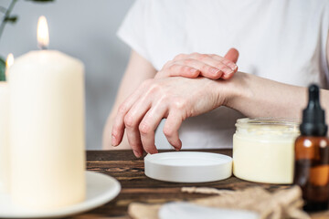 Woman is smearing her hands with a natural organic cream doing a massage. Aroma lamp with essential oils and candles on the table. Concept of skin and self care in atmosphere of harmony and relaxation