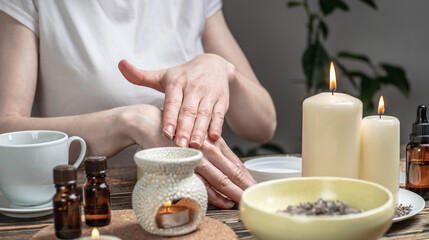 Woman is smearing her hands with a natural organic cream doing a massage. Aroma lamp with essential...