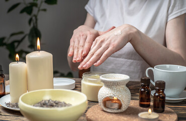 Woman is smearing her hands with a natural organic cream doing a massage. Aroma lamp with essential oils and candles on the table. Concept of skin and self care in atmosphere of harmony and relaxation
