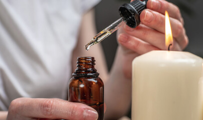 Woman is holding an open bottle of natural oil in her hands and a drop is falling into the bottle....