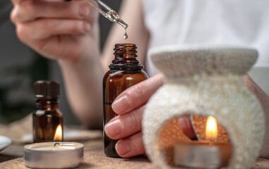 Drop of organic natural oil is dripping into a bottle. There is an aroma lamp, essential oils and...