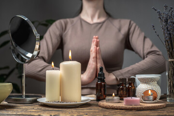 Woman is performing rituals for relaxation. Aroma lamp with essential oils and mirror and burning candles on the table. Concept of meditation, harmony, care procedures in an atmosphere of calmness