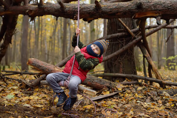 Little boy scout during hiking in autumn forest. Child is swinging on bungee. Adventure, scouting and hiking tourism for kids. - obrazy, fototapety, plakaty