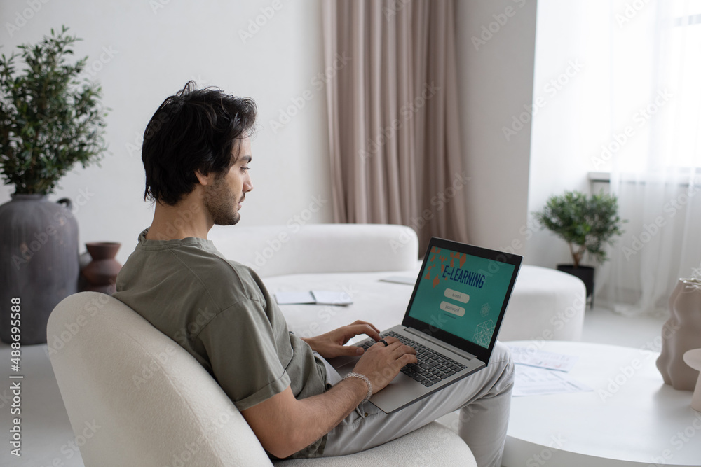 Aufkleber young contemporary man with laptop on knees taking online course of study while sitting on white com