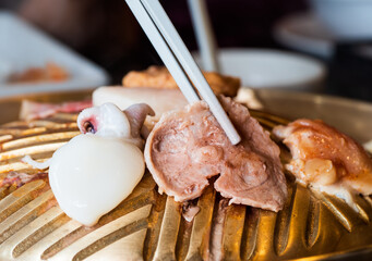 The pork is roasted on a barbeque using white chopsticks, where heat and smoke emanate from the dish.