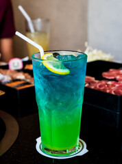 A glass of water containing vibrant green and blue liquids, such as the Blue Ocean. On top, there...