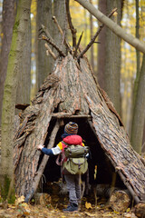 Little boy scout during hiking in autumn forest. Child examining teepee hut in woodland. Concepts...