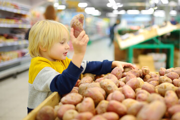 Cute boy is buying fresh organic potatoes in grocery store or supermarket. Child is helper for family. Healthy food for kids.