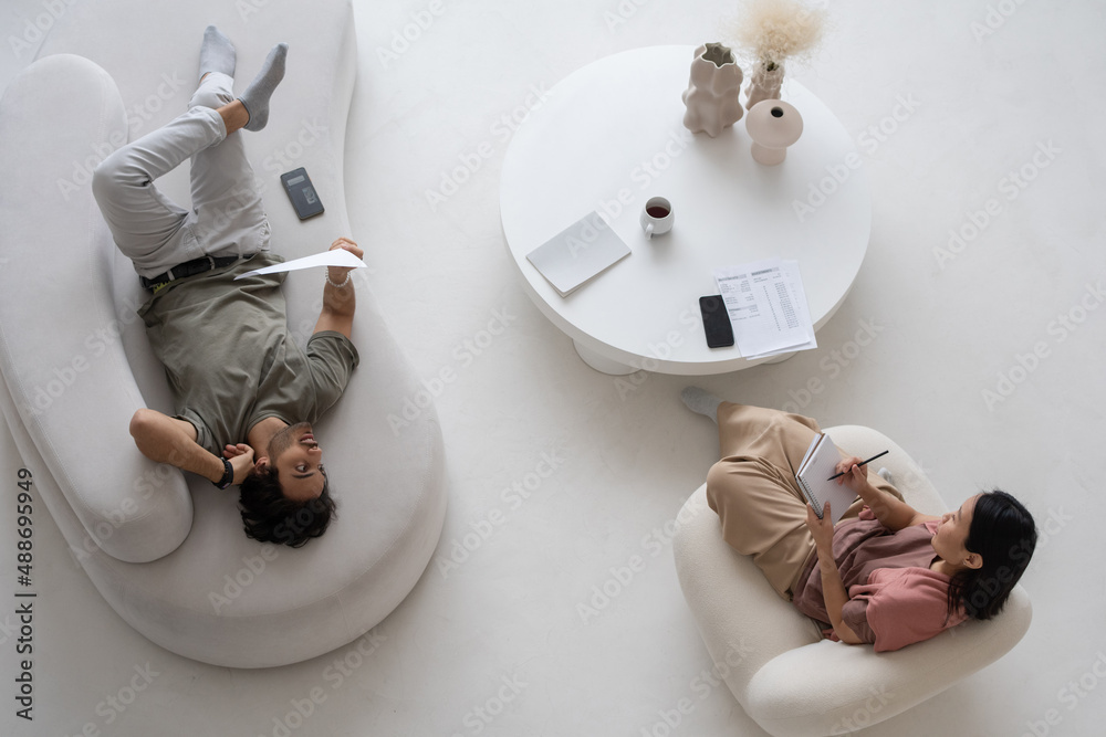 Poster Overview of two young specialists in casualwear discussing financial data while woman making notes and man analyzing information