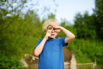 Little boy playing with magnifying glass. Baby carefully looking at you with magnifier. Activity for inquisitive child. Charming kid exploring nature with loupe.