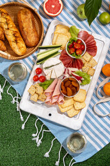 Picnic blanket with charcuterie boards, healthy food and wine in park on the grass on sunny day.