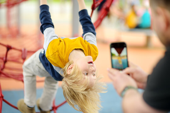 Father is taking a shot of his son having fun during stroll on outdoor playground. Active sport leisure for family with kids. Photo or video for blog, diary or messenger.
