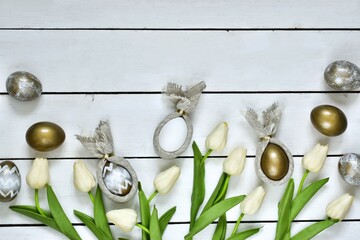Happy Easter. Decorated Eggs, white tulips and Easter bunnys made of napkins on a white wooden background. Top view. Easter composition with copy space