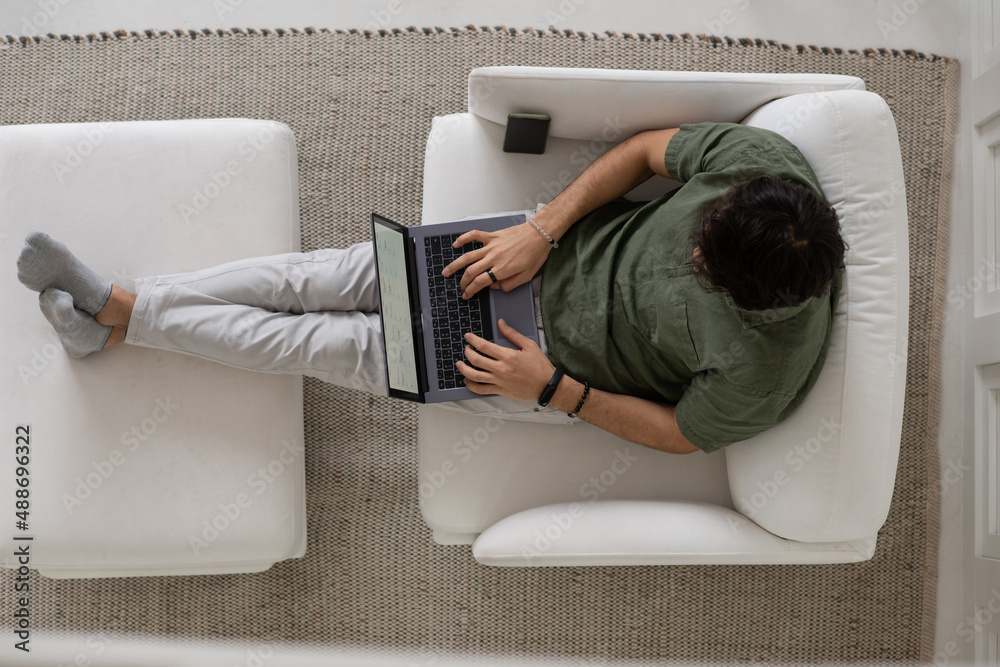 Poster overview of young male employee typing on laptop keyboard while looking through graphic data and ana