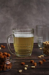 light beer in a glass mug with crackers and peanuts on a dark background