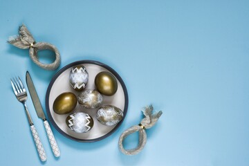 Easter background with Easter decorative eggs. Easter composition with eggs on plate and cutlery on blue background. Easter bunny napkin gift egg wrapping idea. Flat lay composition with copy space 