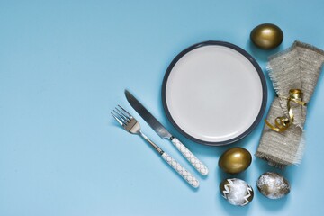 Easter table setting with decorative eggs, plate, napkin and cutlery on blue table. Elegance dinner. Top view. Space for text. Holidays background. Easter table.