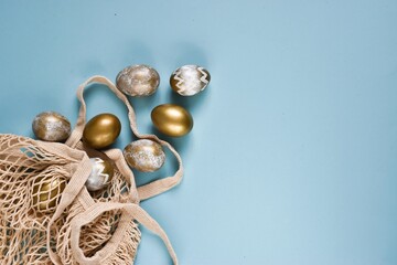 Golden, white Easter eggs in a stringed cotton bag on a blue background. Geometry. Minimal concept. View from above. Card with copy space for text. Concept - promotion, sale, shopping