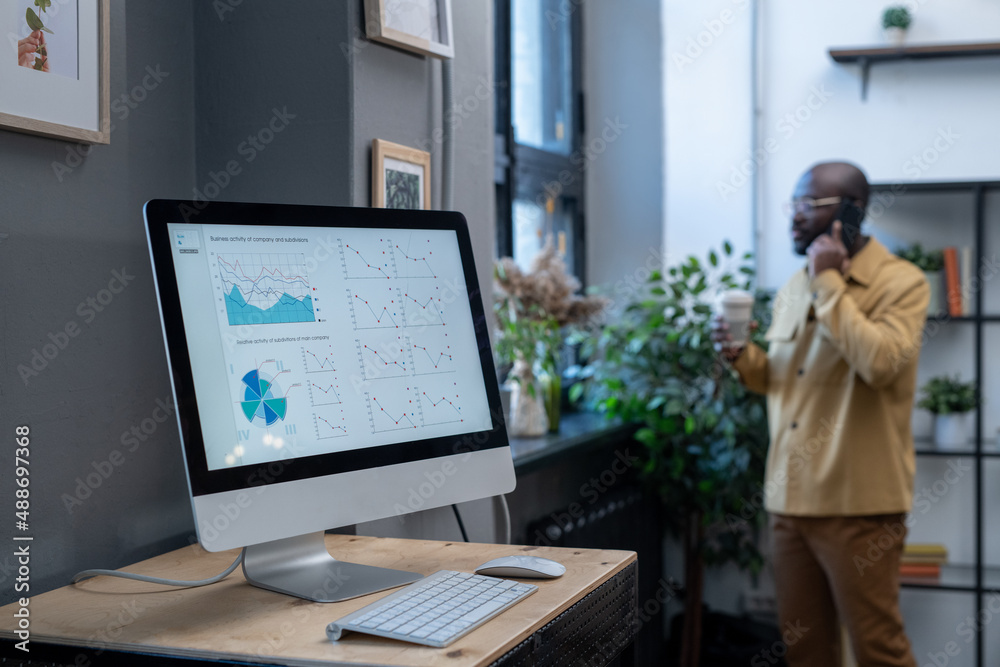 Poster Computer monitor on desk with digital financial diagram and graphs on screen on background of young businessman calling