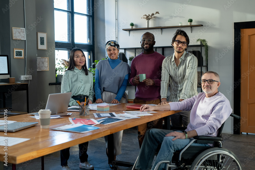 Poster Group of happy modern economists standing in row in front of table with financial papers in urban office and looking at camera