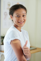 Portrait of happy girl with bandage on her arm after injection, she gesturing she ok while standing...