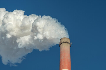 Powerful industrial factory chimney is smoking and polluting the environment with carbon dioxide