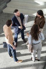 Young coworkers in formalwear standing inside large office center and having discussion of working points and new ideas for project