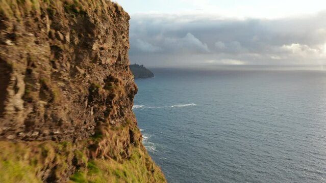 Forwards fly around rock wall. Revealing beautiful scenery of high vertical cliffs at sea coast. Cliffs of Moher, Ireland