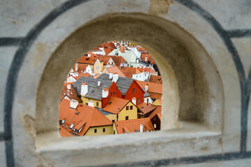 View through a window in the wall onto the roofs of houses with two red houses in Český Krumlov in the Czech Republic