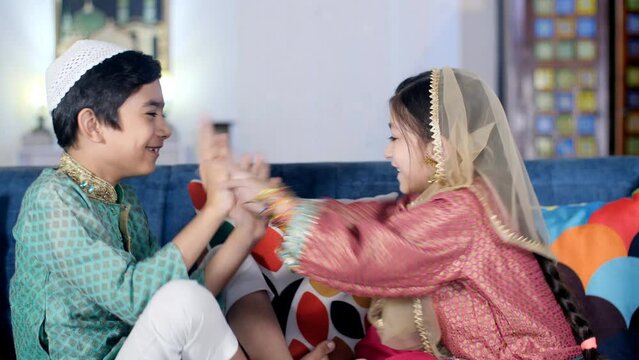 Happy Muslim kids having fun while playing patty-cake hand-clapping games. Joyful Indian siblings doing a leisure activity while sitting on the couch at home - family bonding  relaxation  a happy c...