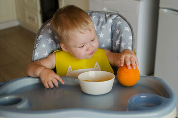 A little baby eats an orange at a children's table