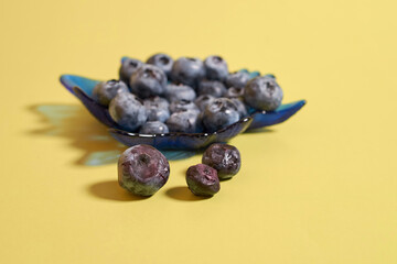 Ripe and rotten blueberries in a glass plate on a colored background